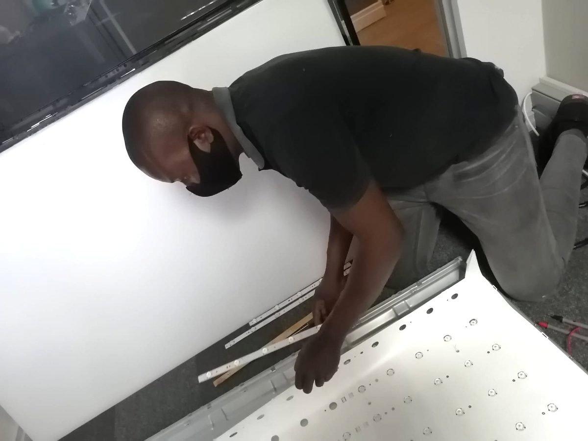 Technician kneeling beside an open television panel, fitting new LED backlight strips